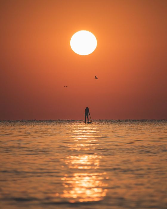 Снимка на момиче с падълборд на фона на изгряващото слънце над Черно море.